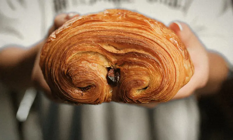 A flaky pain au chocolat held out in two hands